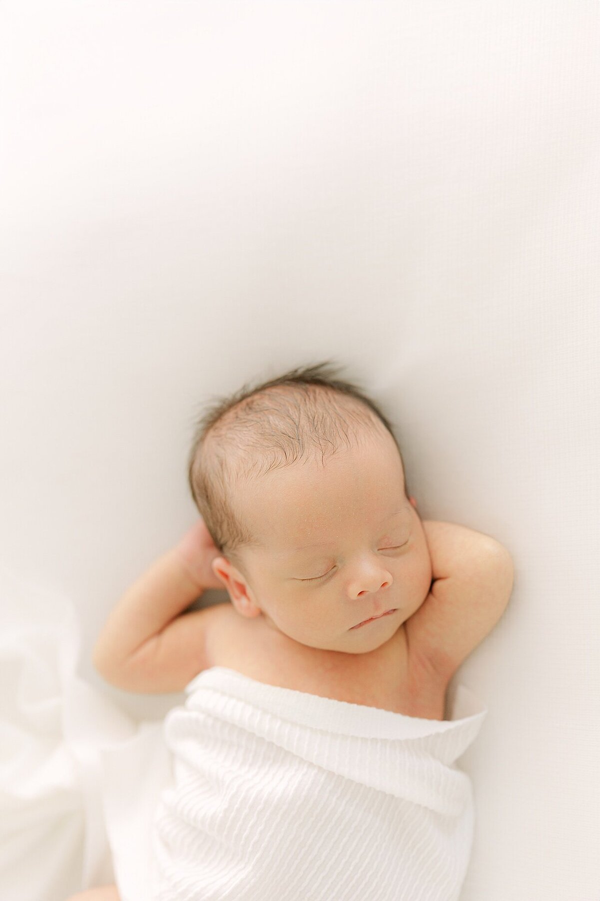 Portrait of a sleeping newborn's face with his hands behind his head during an Indianapolis newborn photography session