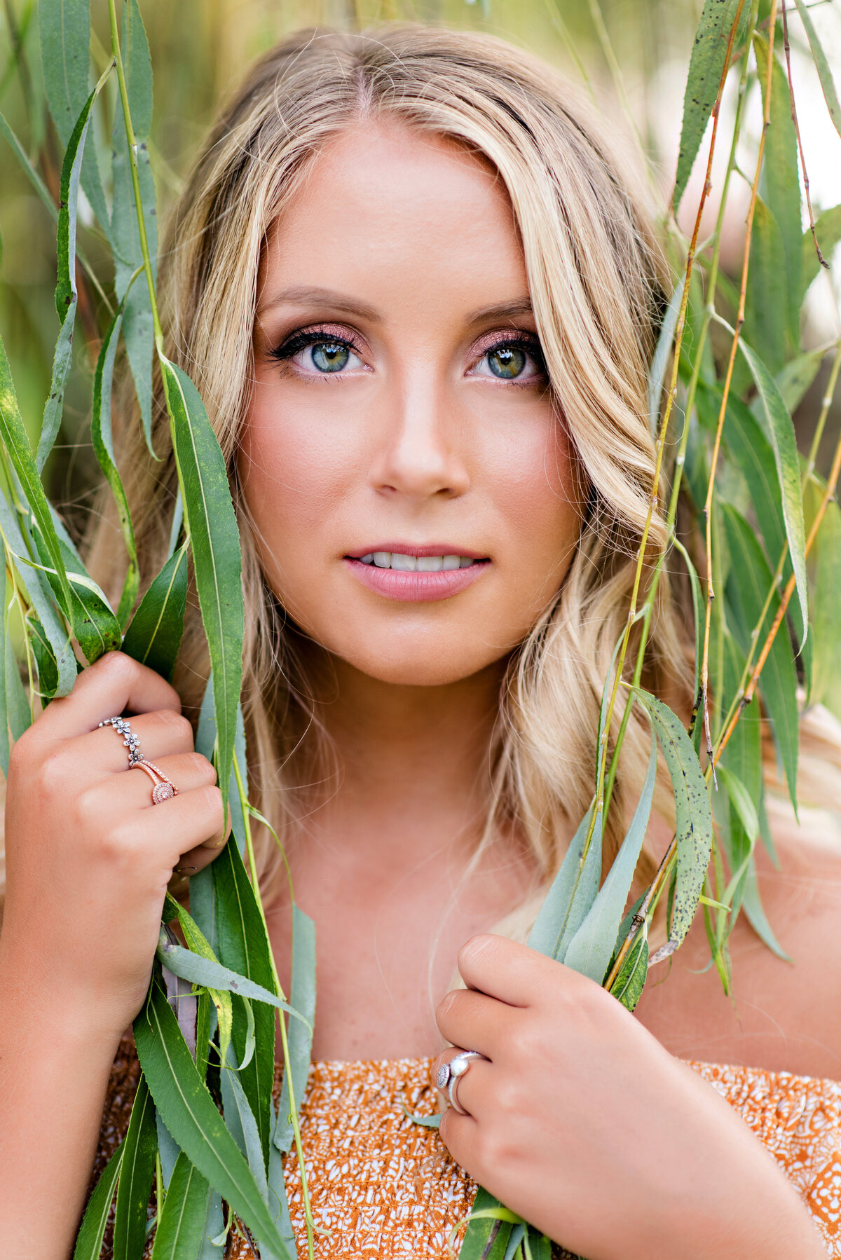 High school senior girl poses in willow tree at Amber Grove venue for her high school senior portrait session.