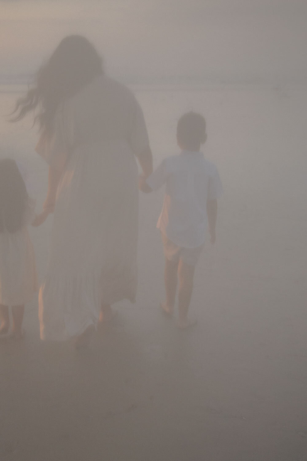 A mother holding hands with her children walking along a foggy beach