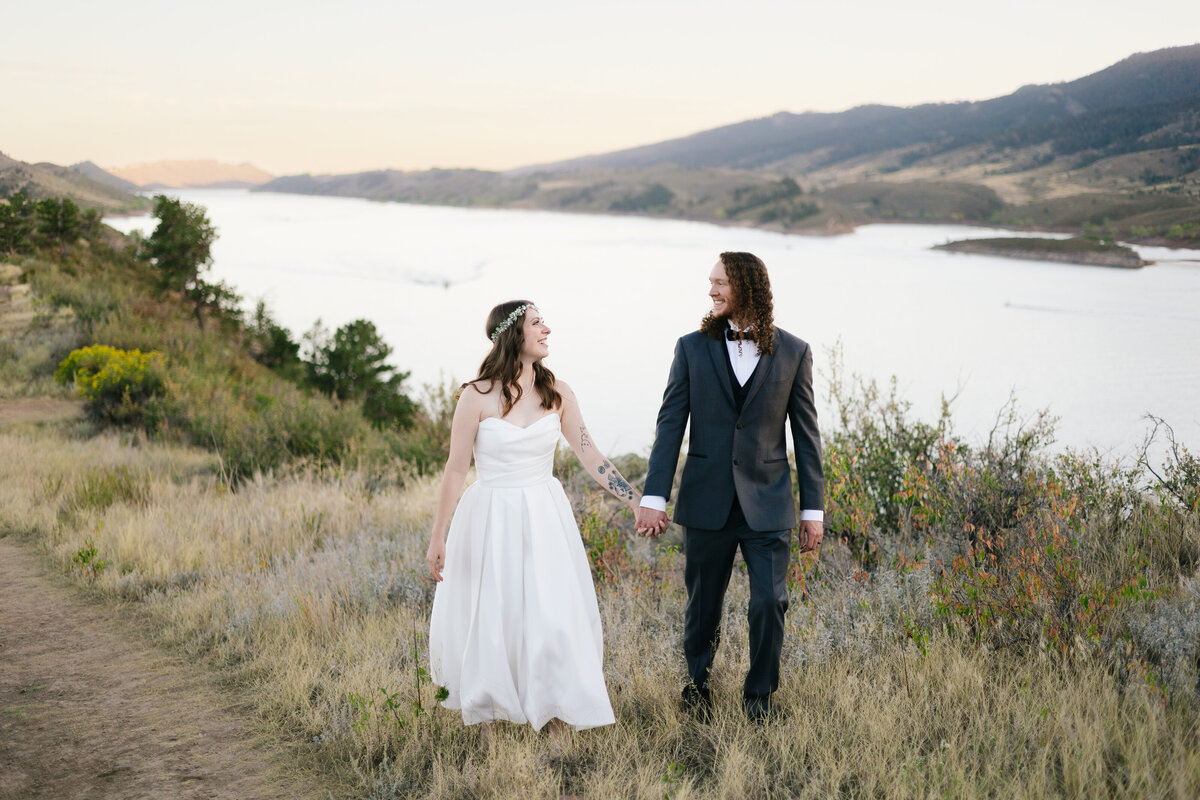 A couple holding hands while standing near the scenic shores of Horsetooth Reservoir, celebrating their elopement in Fort Collins, Colorado.