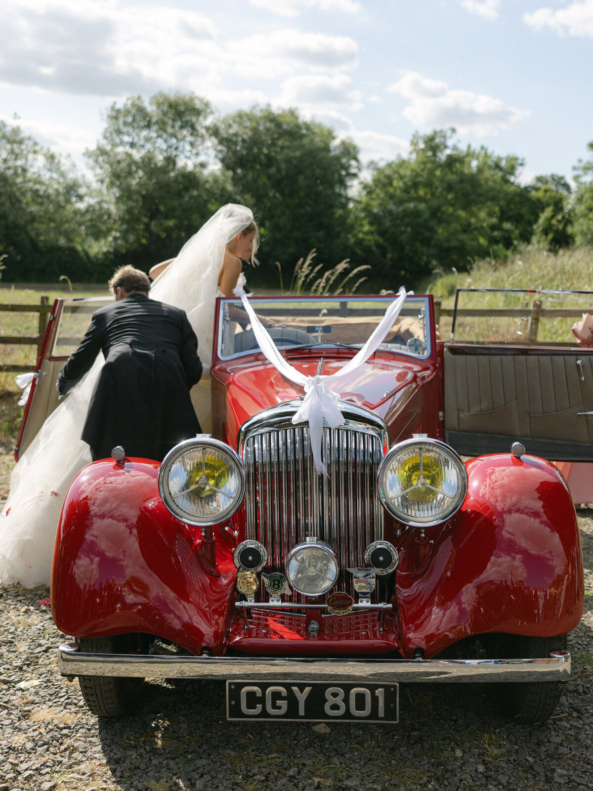 Groom helping bride in vintage red car.