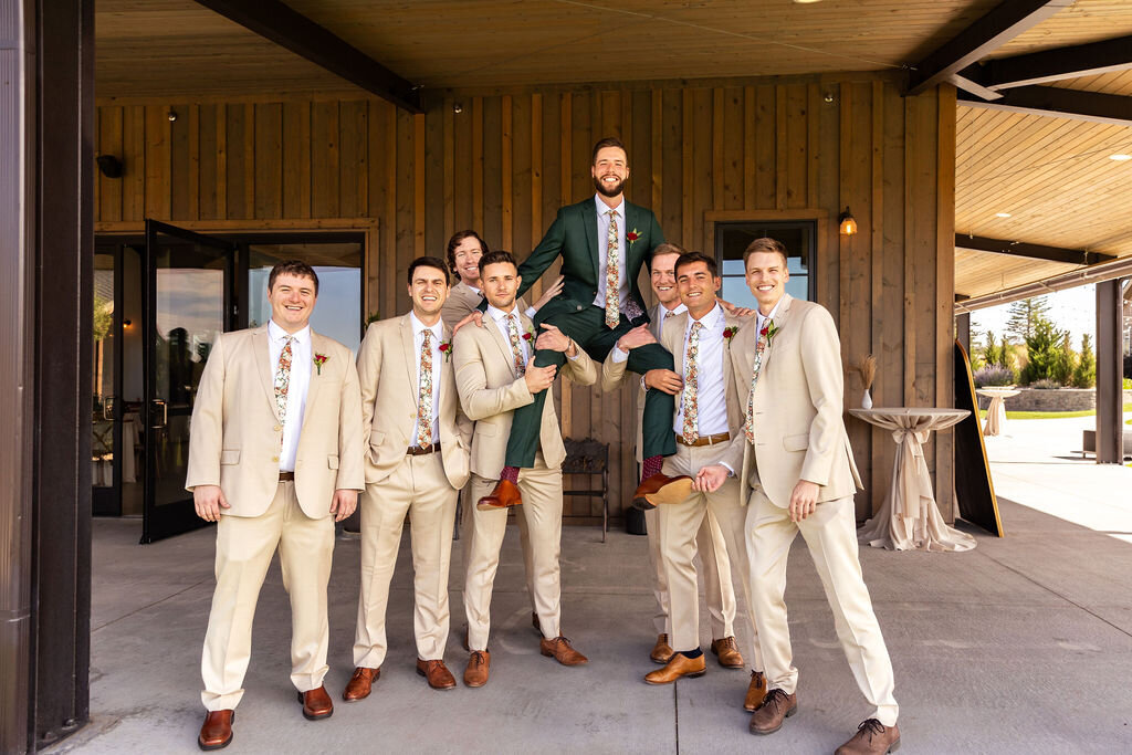 Groom in a dark green suit poses with his groomsmen in tan suits.