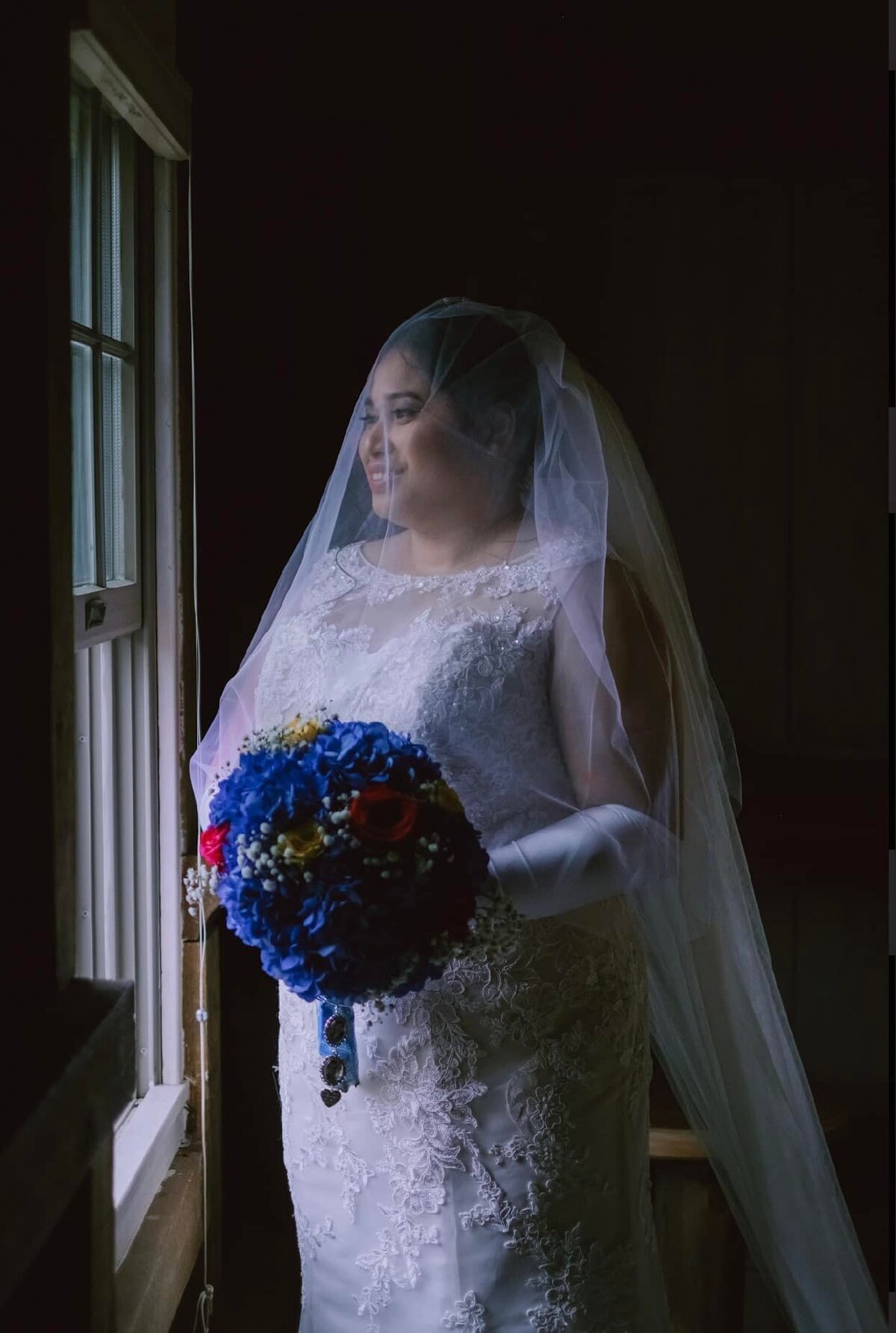 Smiling bride looking through a window in her white wedding dress and blue bouquet.