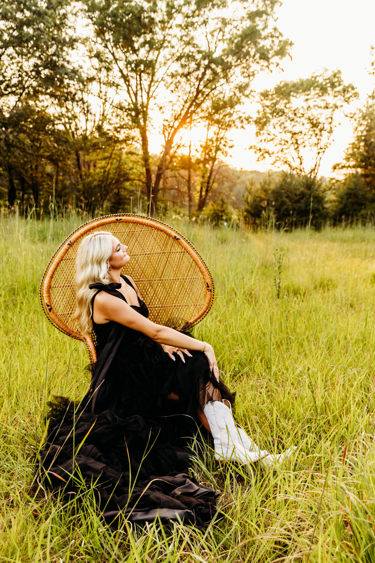 gorgeous high school girl in a fluffy black dress sitting with her legs crossed on a peacock chair with her white boots sticking out. 