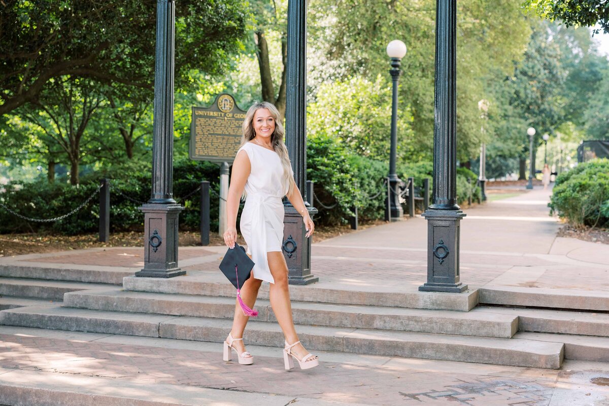 girl in white dress with graduation cap walks under the Arch at University of Georgia