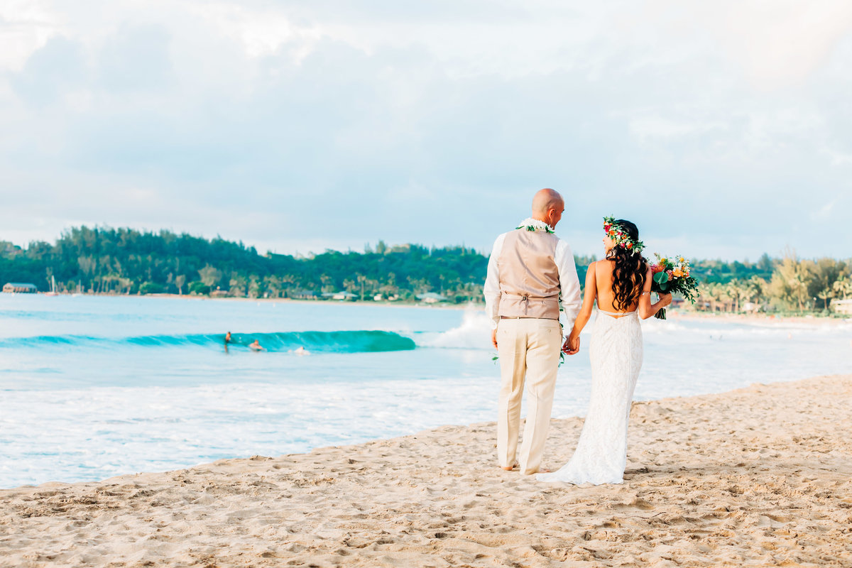 bride and groom walking away on the beach at Hanalei Bay in Kauai