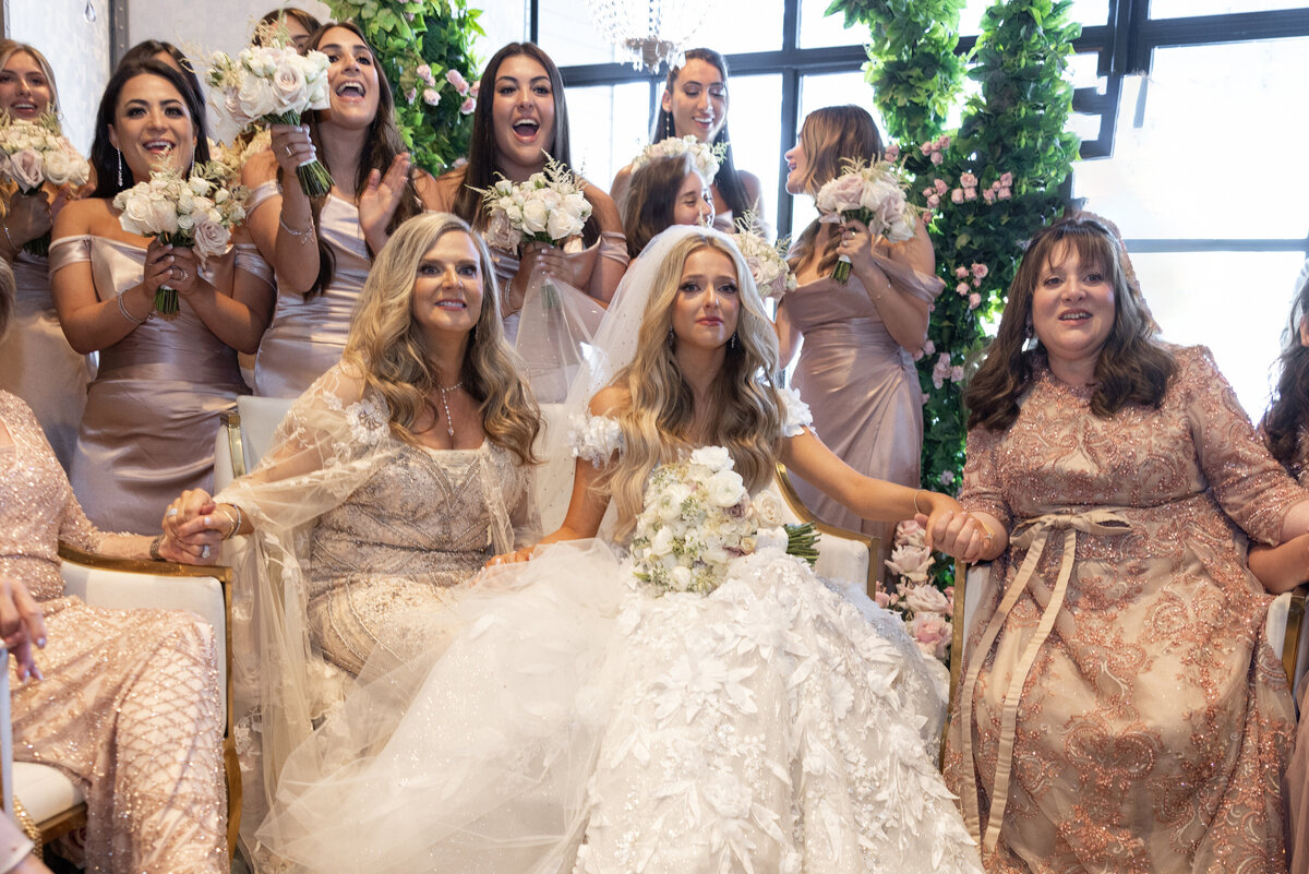 A bride sitting down with her bridesmaids standing behind her