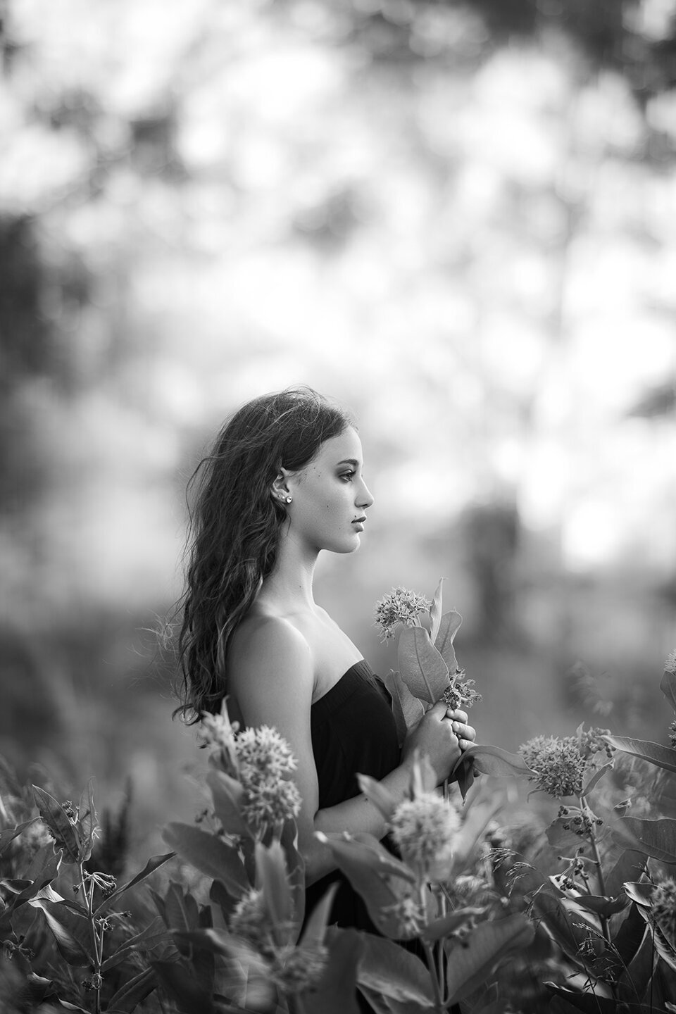 black and white photo of girl in milk weed flowers in billings montana, located at joels pond near sunset.