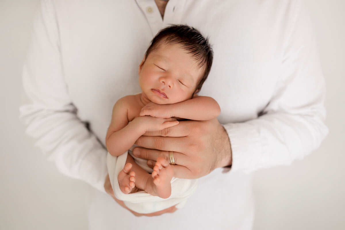 Close-up of a newborn baby sleeping peacefully in a parent's arms, with the parent wearing a white shirt.