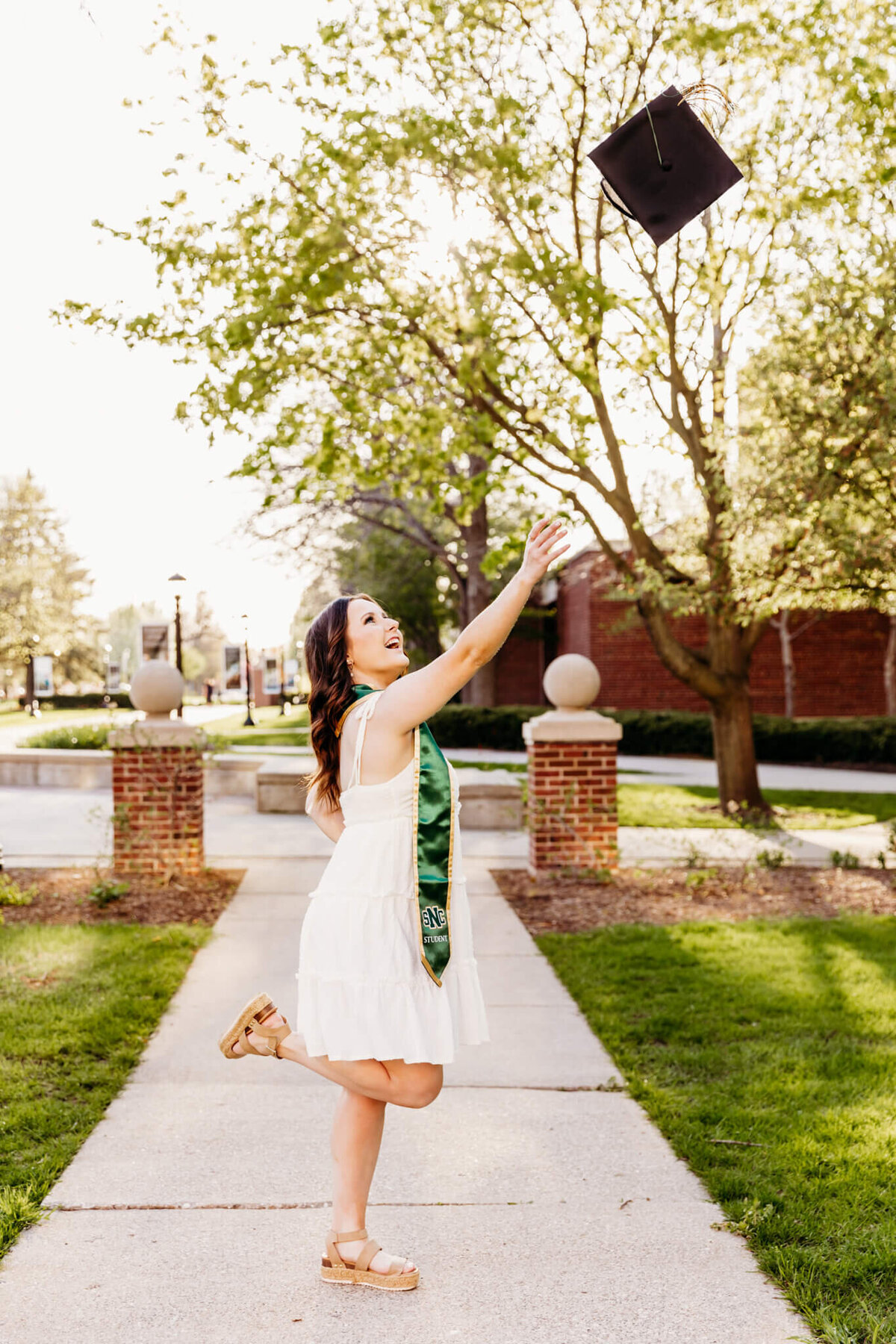 Beautiful St Norbert college grad throwing her graduation cap in the air and kicking her foot up as she enjoys her college graduation photo sessioni