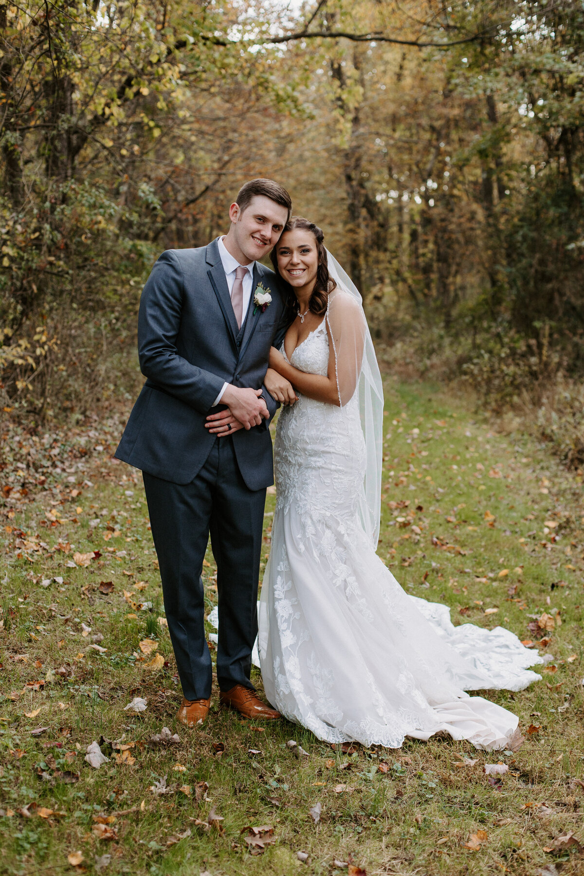 bride and groom with their arms linked smiling in a wooded area