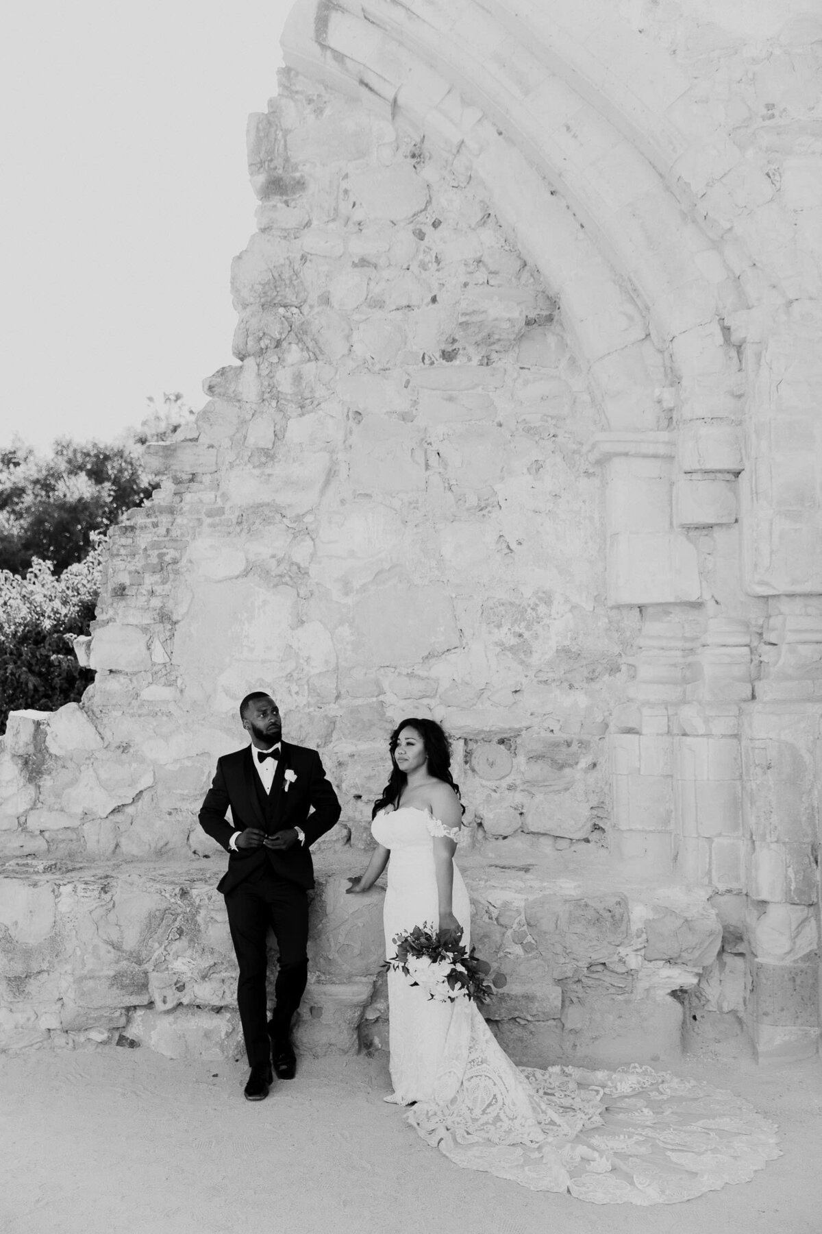 Groom and Bride posing in front of wall at Mission San Juan Capistrano