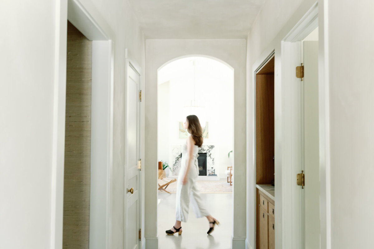 designer in beige linen jumpsuit, movement photography, walks under arch at Fernhaus, Northern Michigan
