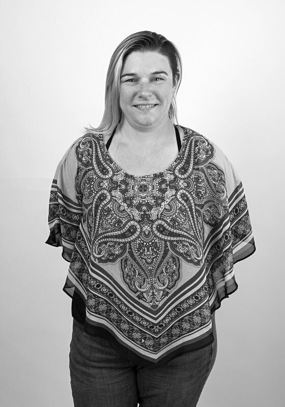 Black and white before shot of a tattooed woman in a tank top, standing confidently against a white backdrop.