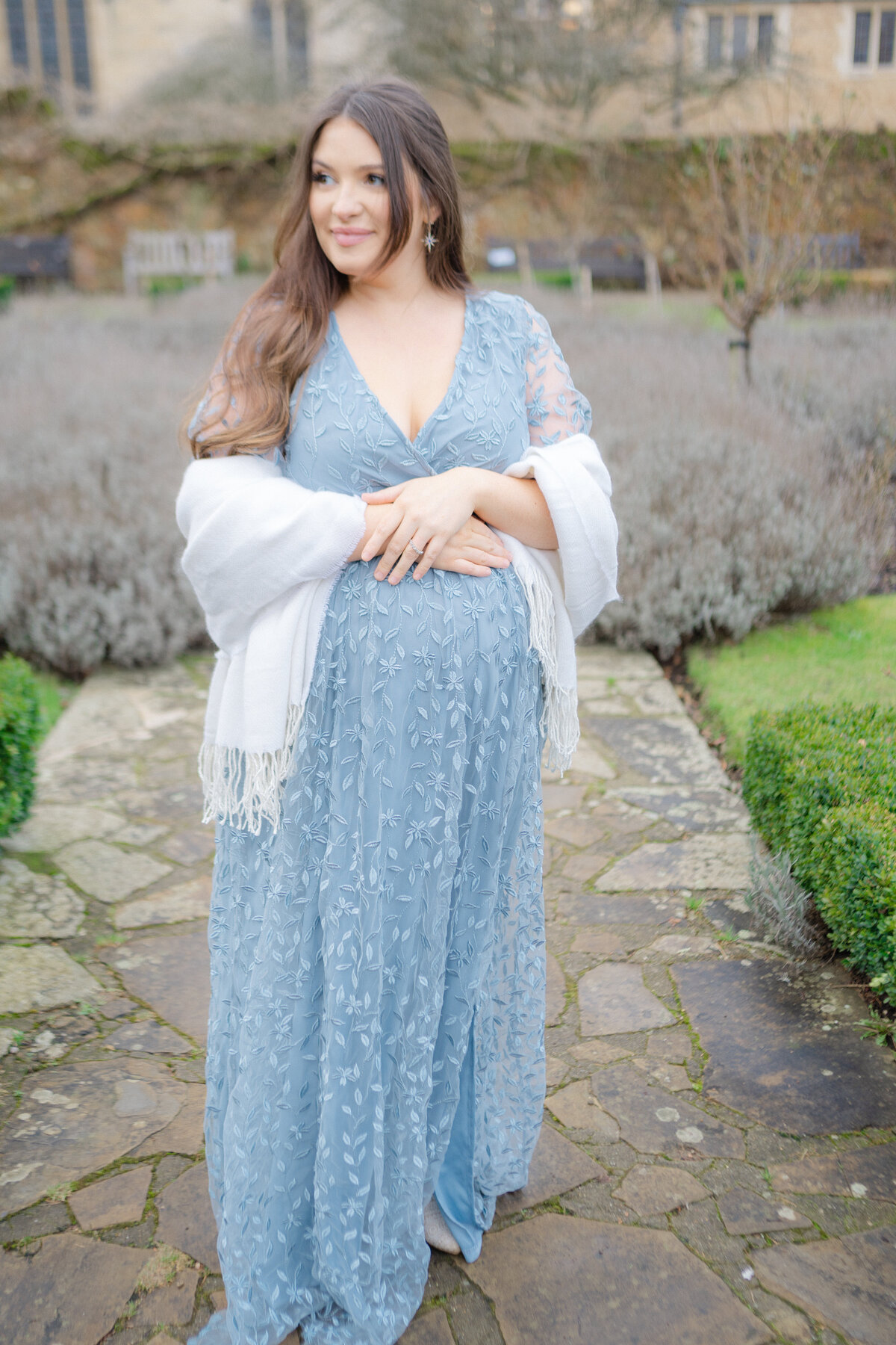 Portrait shot of mother wearing a needle and thread gown with her hands crossed on her bump and standing in the middle of a garden square by Maternity Photographer Courtney Cronin in Oklahoma City