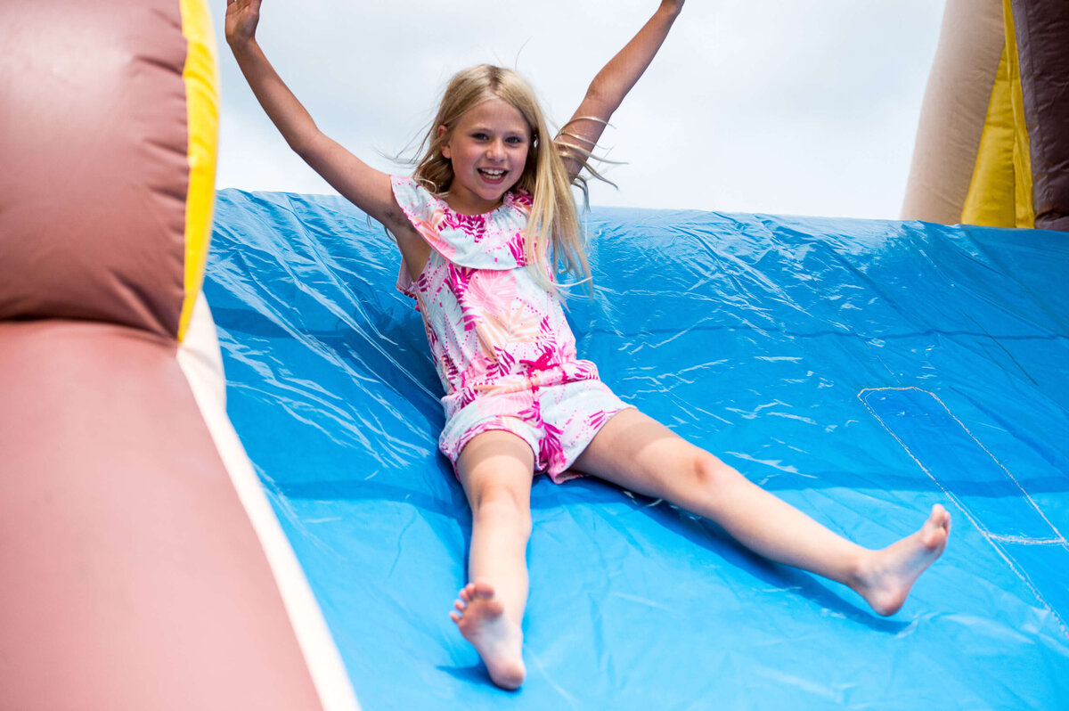 a young girl in a pink shorts outfit sliding down an inflatable slide.  Captured by Ottawa Event Photographer JEMMAN Photography COMMERCIAL during a corporate children's event