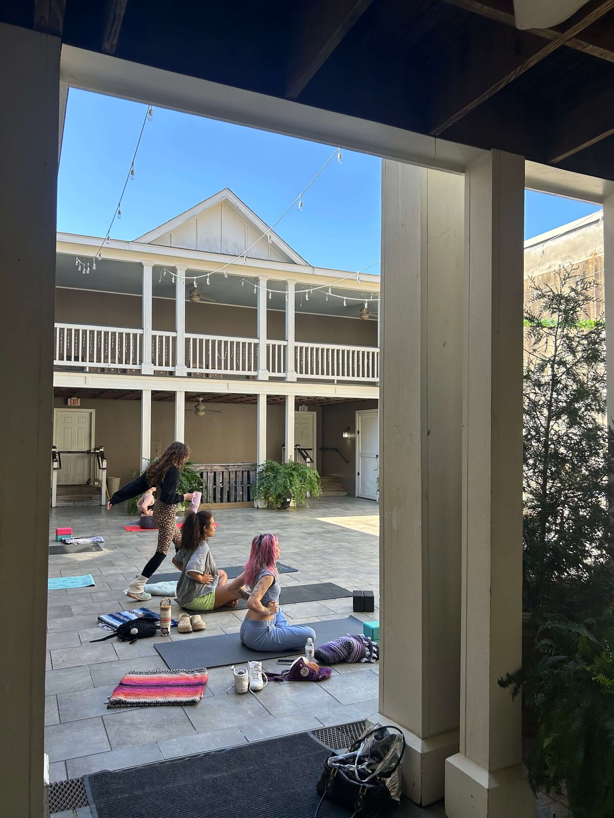 A group of women get set up for a yoga event in a brightly lit courtyard.