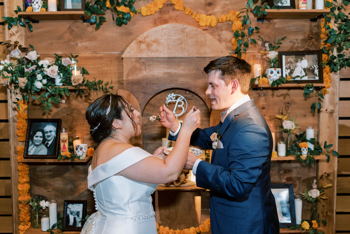 Bride and groom feeding each other wedding cake in front of a custom wooden backdrop display