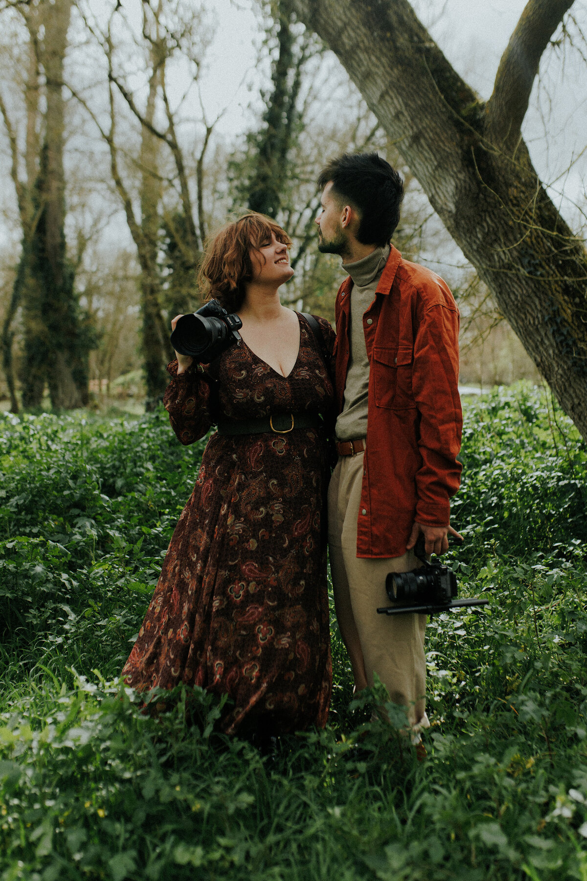 Léa et Nolan, photographe et vidéaste mariage posant dans la forêt avec leurs appareils.
