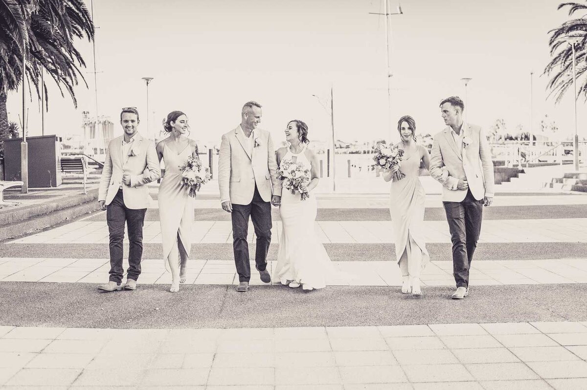 Black and white wedding photo of a couple walking with their bridal party.