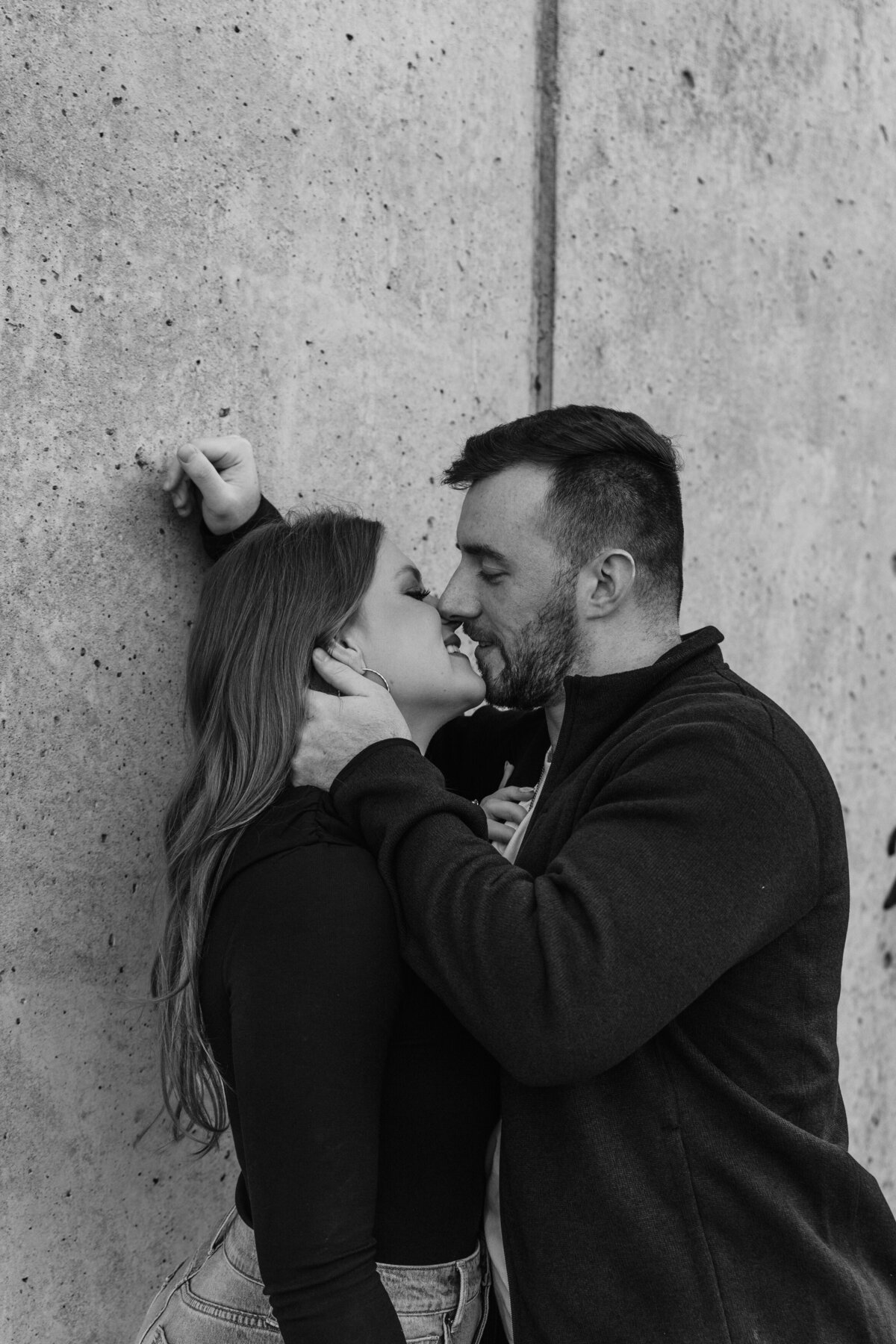 A couple leaned up against a wall as they are about to kiss