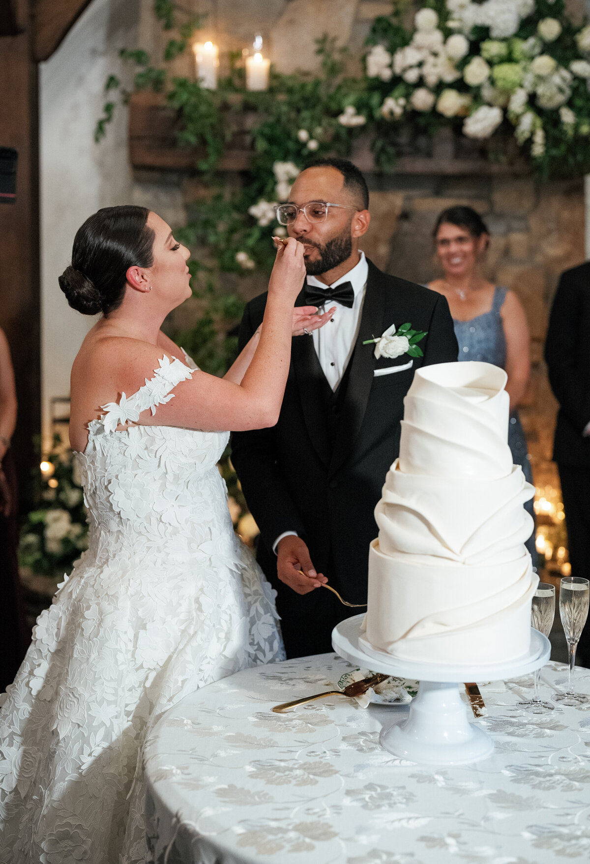 The bride and groom share their wedding cake during their fall Castle Ladyhawke reception, surrounded by candlelight and lush white florals.


