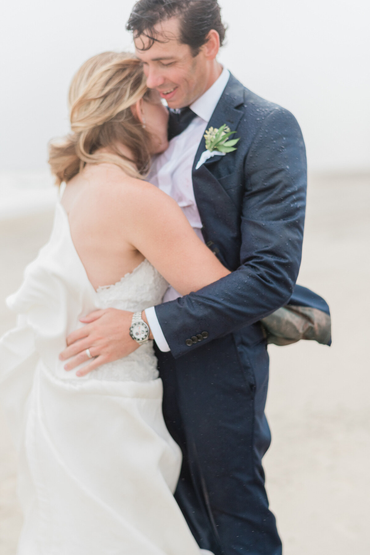 The newlyweds share a warm embrace on the beach as raindrops land on the groom’s navy blue suit. 