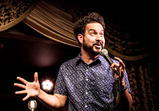 Comedian, Ahmed Bharoocha, holding a microphone and doing stand up comedy