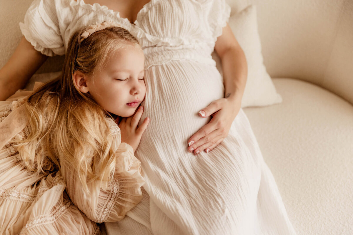 Girl snuggles her mother's baby bump.