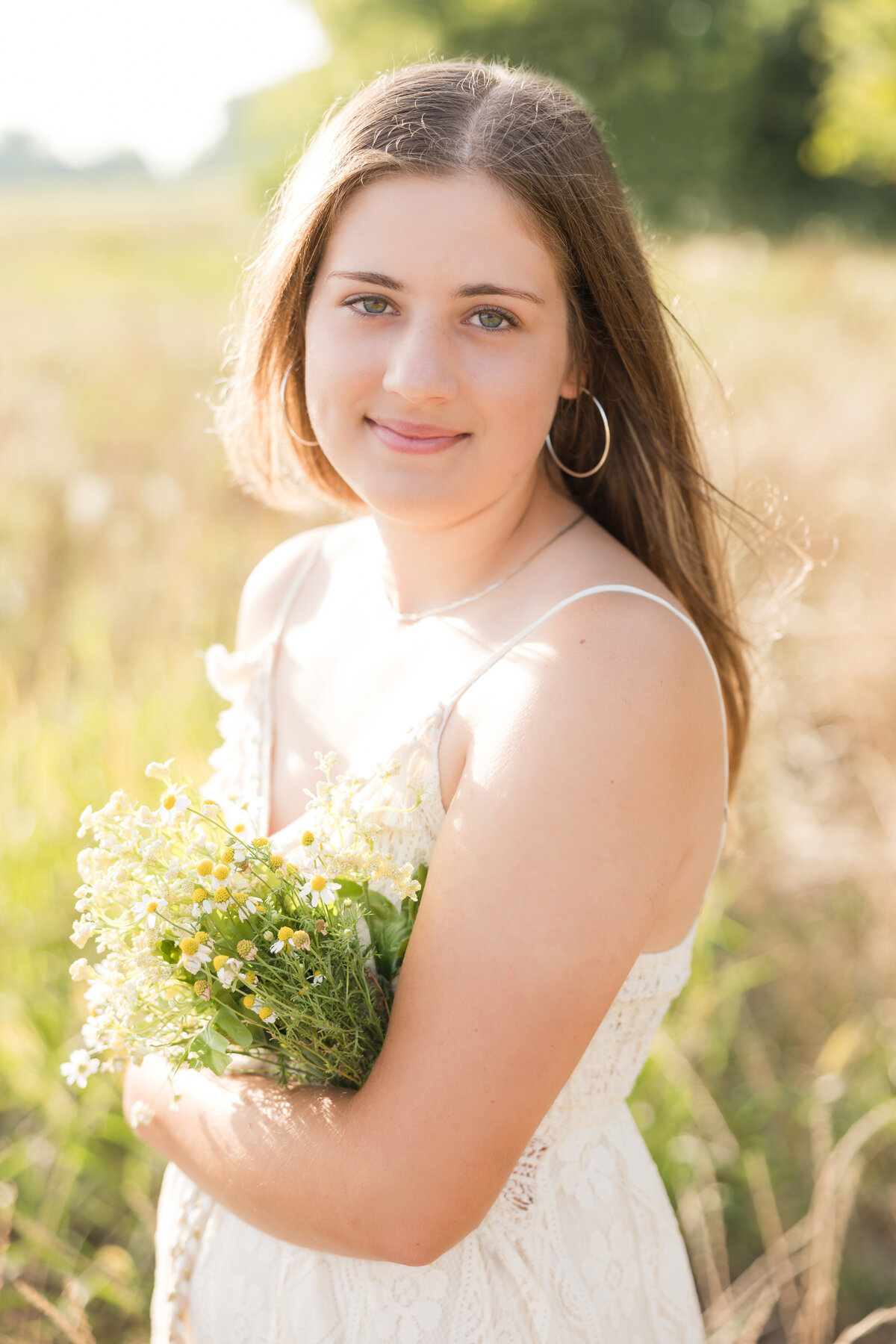 Senior girl in a field holding flowers and smiling at the camera