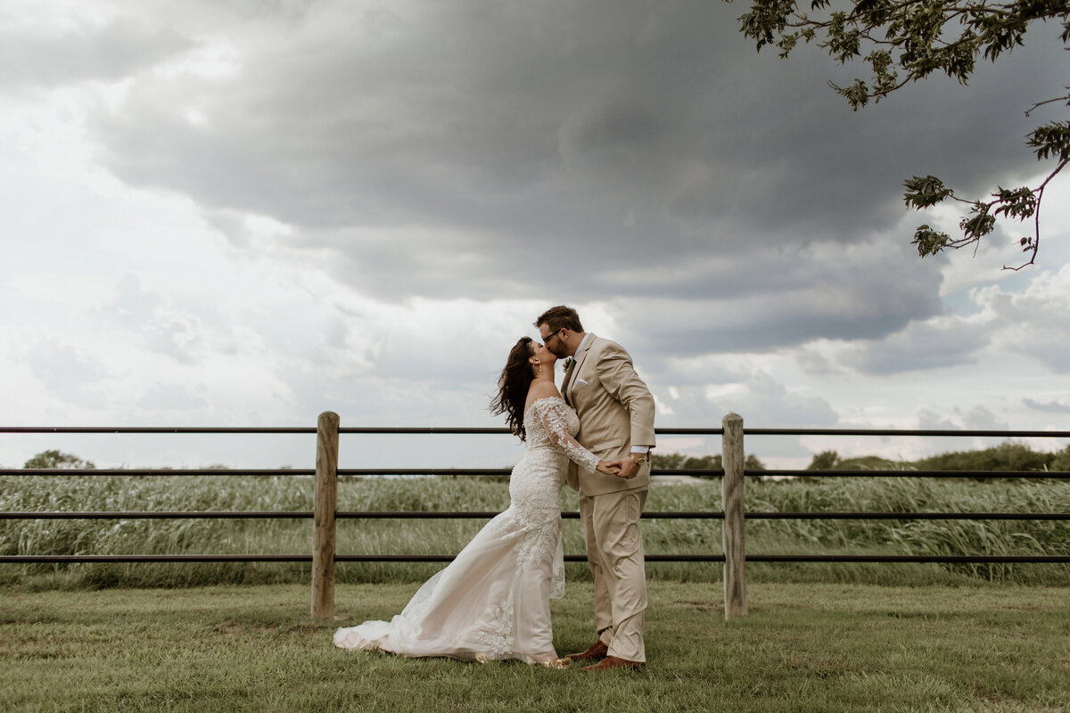 A bride and groom kiss as a storm rolls in at Pecan Creek Farm in Venus Texas. Captured by Fort Worth Wedding Photographer, Megan Christine Studio