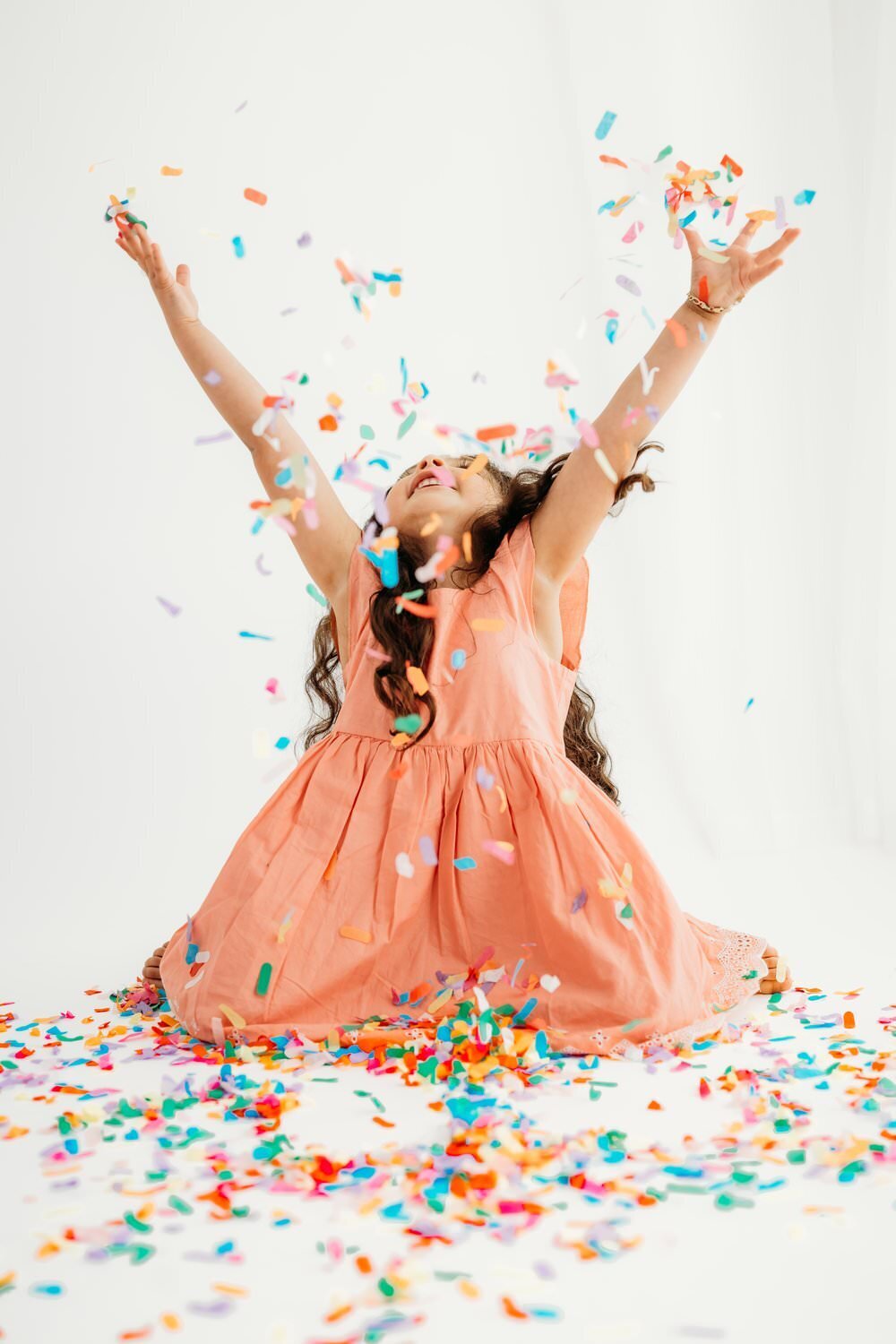 girl throws rainbow confetti in the air on a white studio backdrop