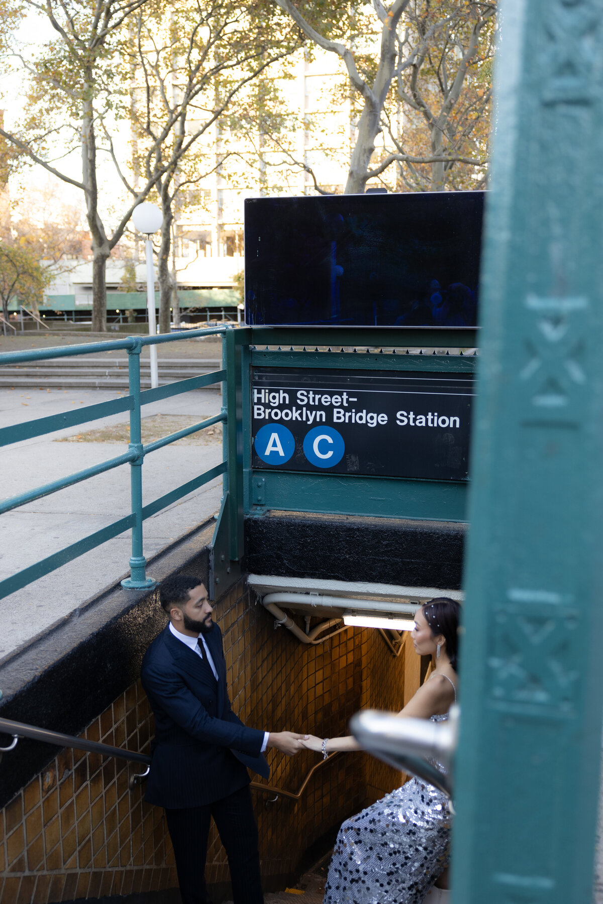 The couple shares a playful laugh on the subway platform, surrounded by the urban energy of New York City.