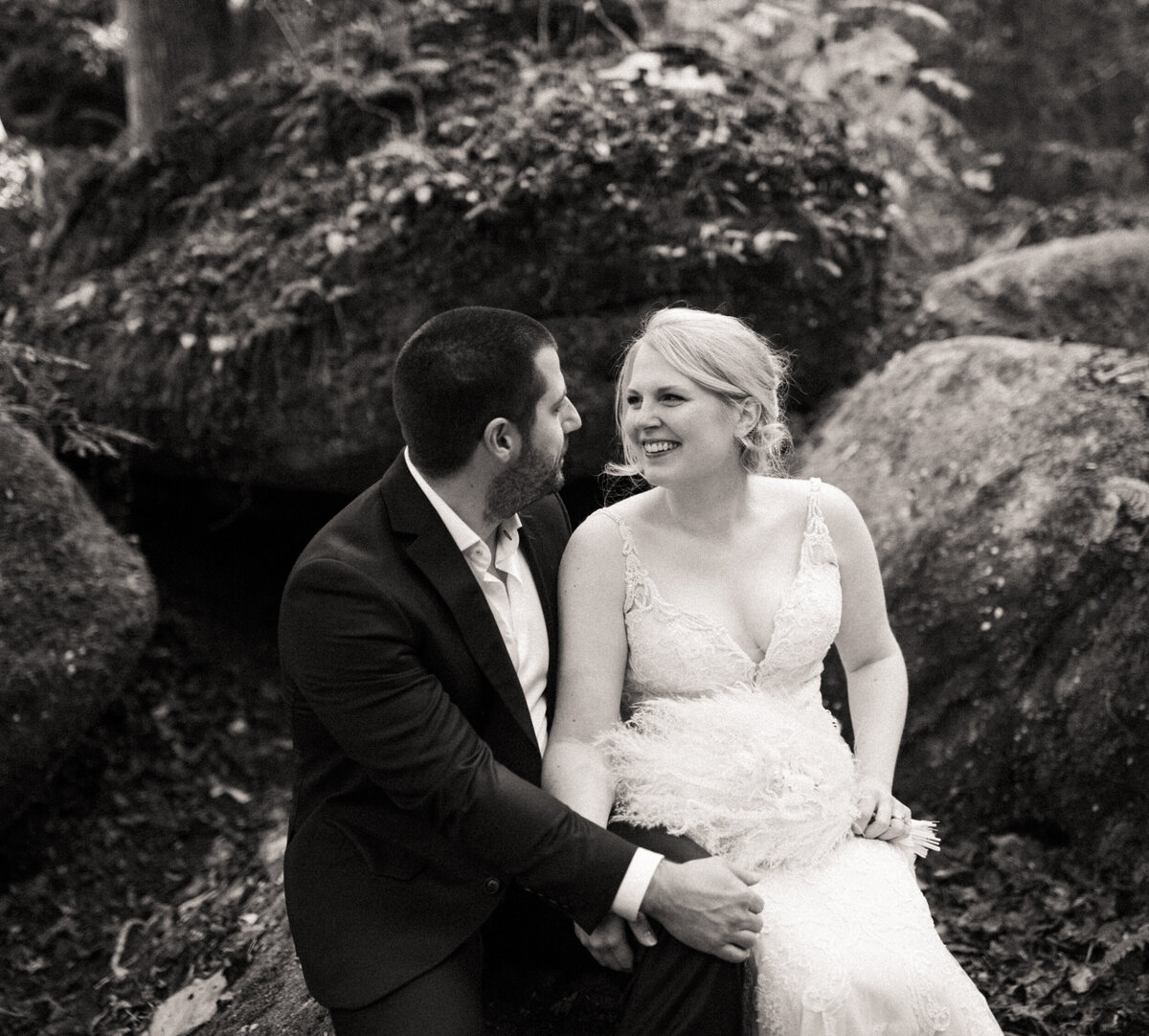 Bride and groom sharing a laugh as they sit on a rock in the forest