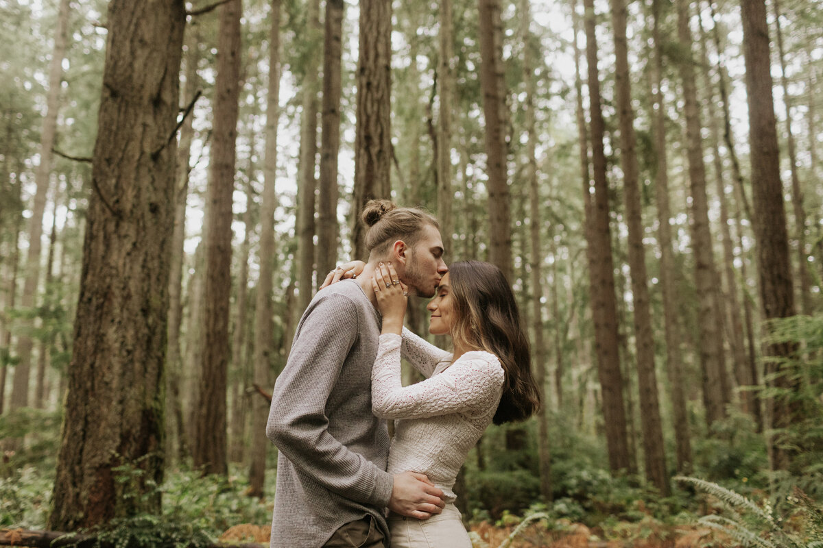 Couple kisses forehead in woods