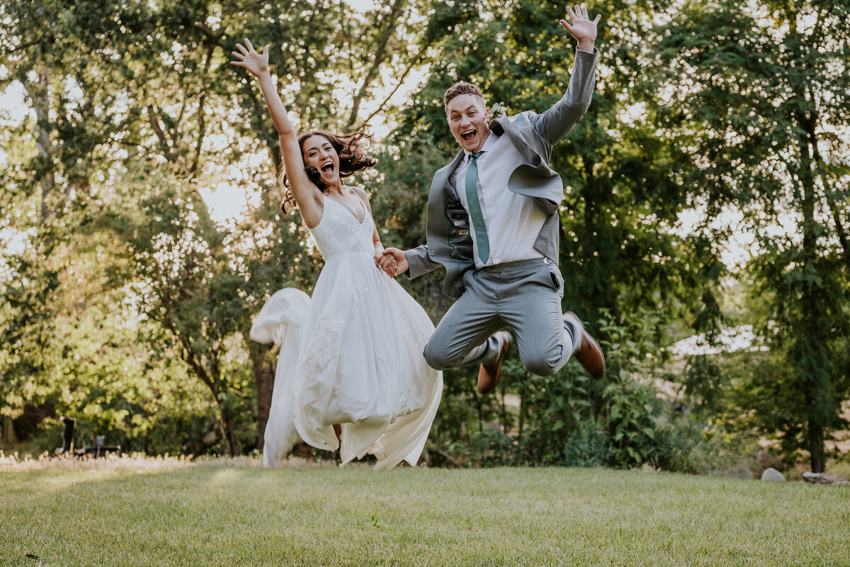 Bride and groom jump in the air while holding hands and smiling.