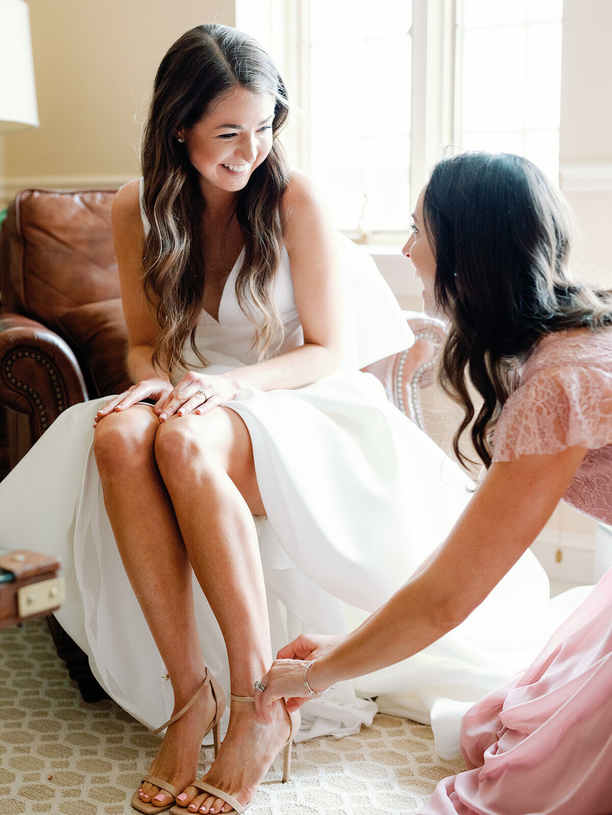 Bride and sister share a moment looking at eachother while she helps bride with her shoes.