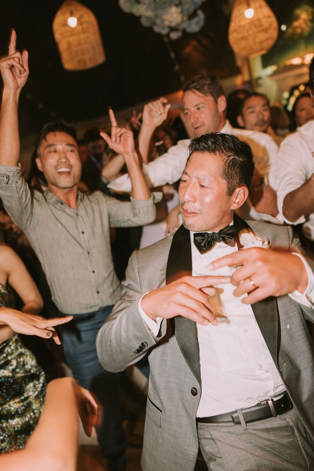 groom with hands up dancing under lantern light at lanikuhonua reception