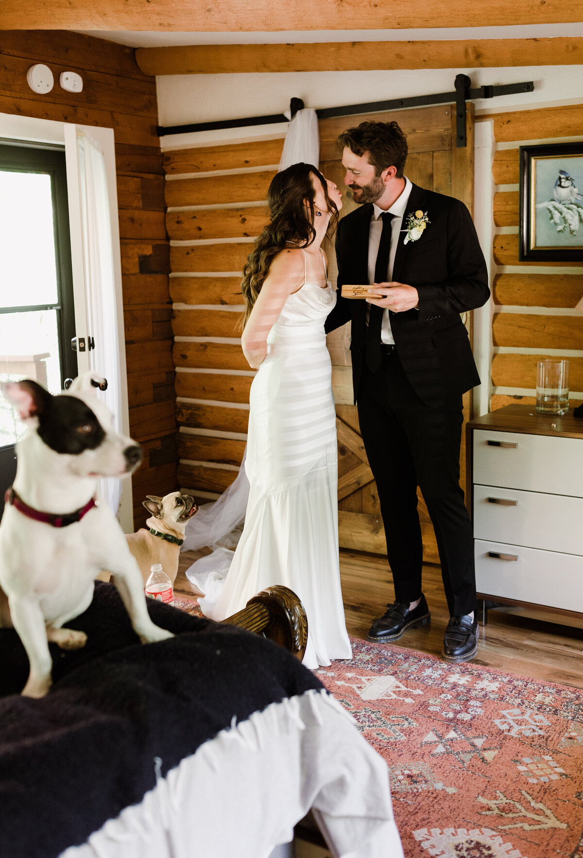 Dog sitting on bed whilst bride and groom kiss in the background