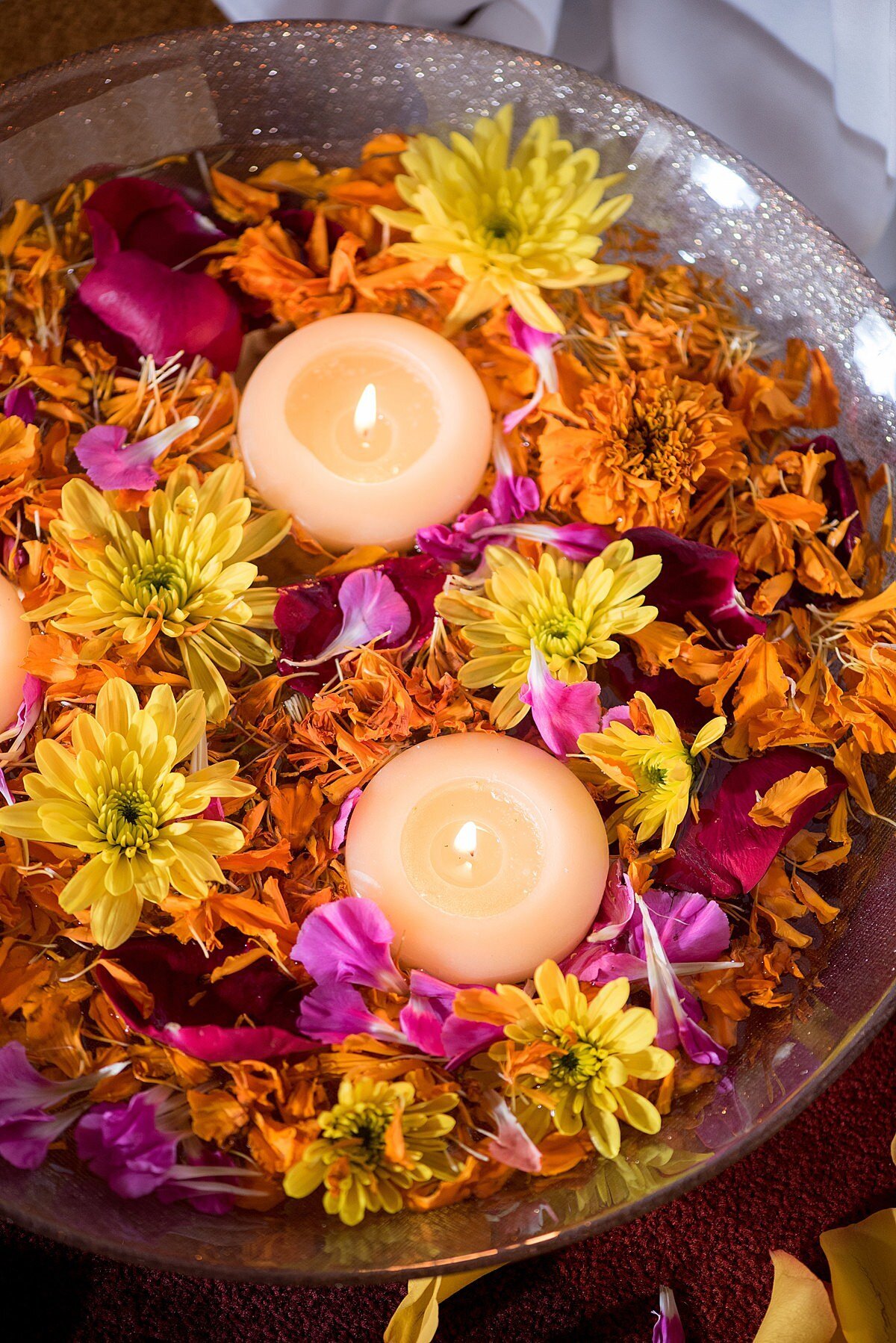 Large glass bowl of water filled with floating candles, pink, yellow and orange flowers for a Hindu wedding