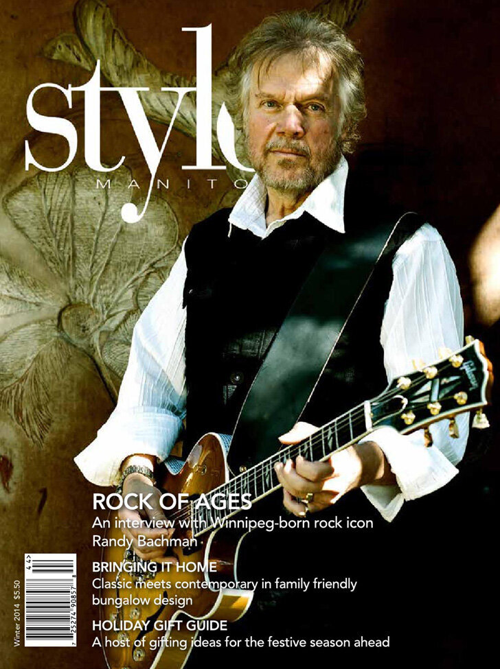 Randy Bachman Style Manitoba Magazine cover standing against etched wood wall holding guitar