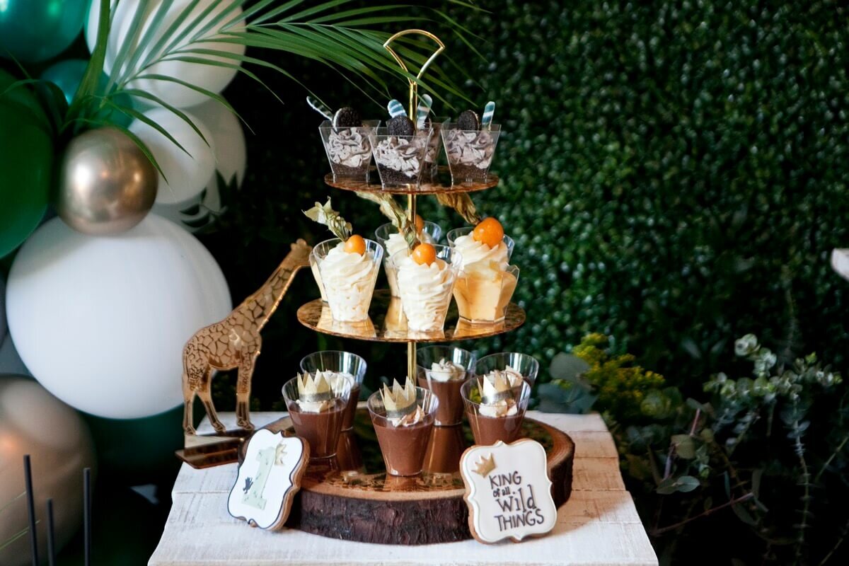 Jungle themed childrens 1st birthday party dessert stand with desserts, cookies and a model giraffe