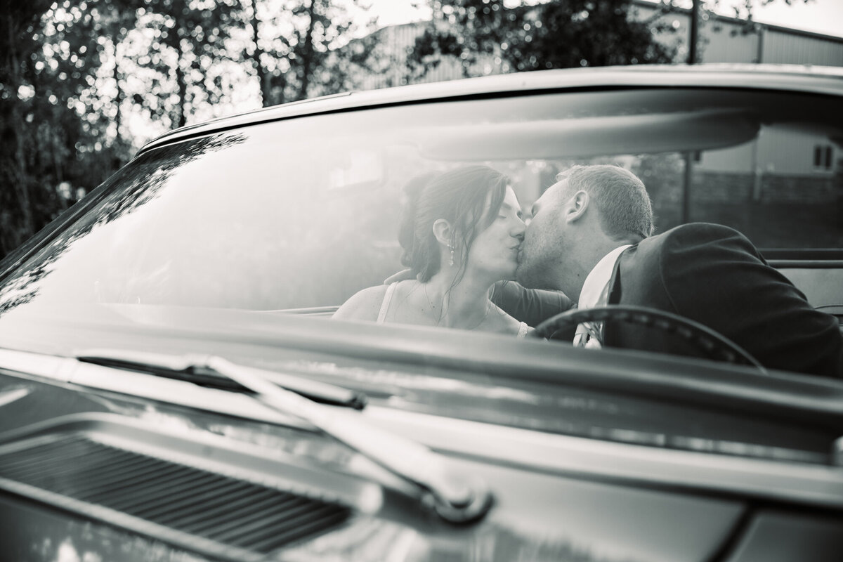 bride and groom kiss as photo is captures through windshield