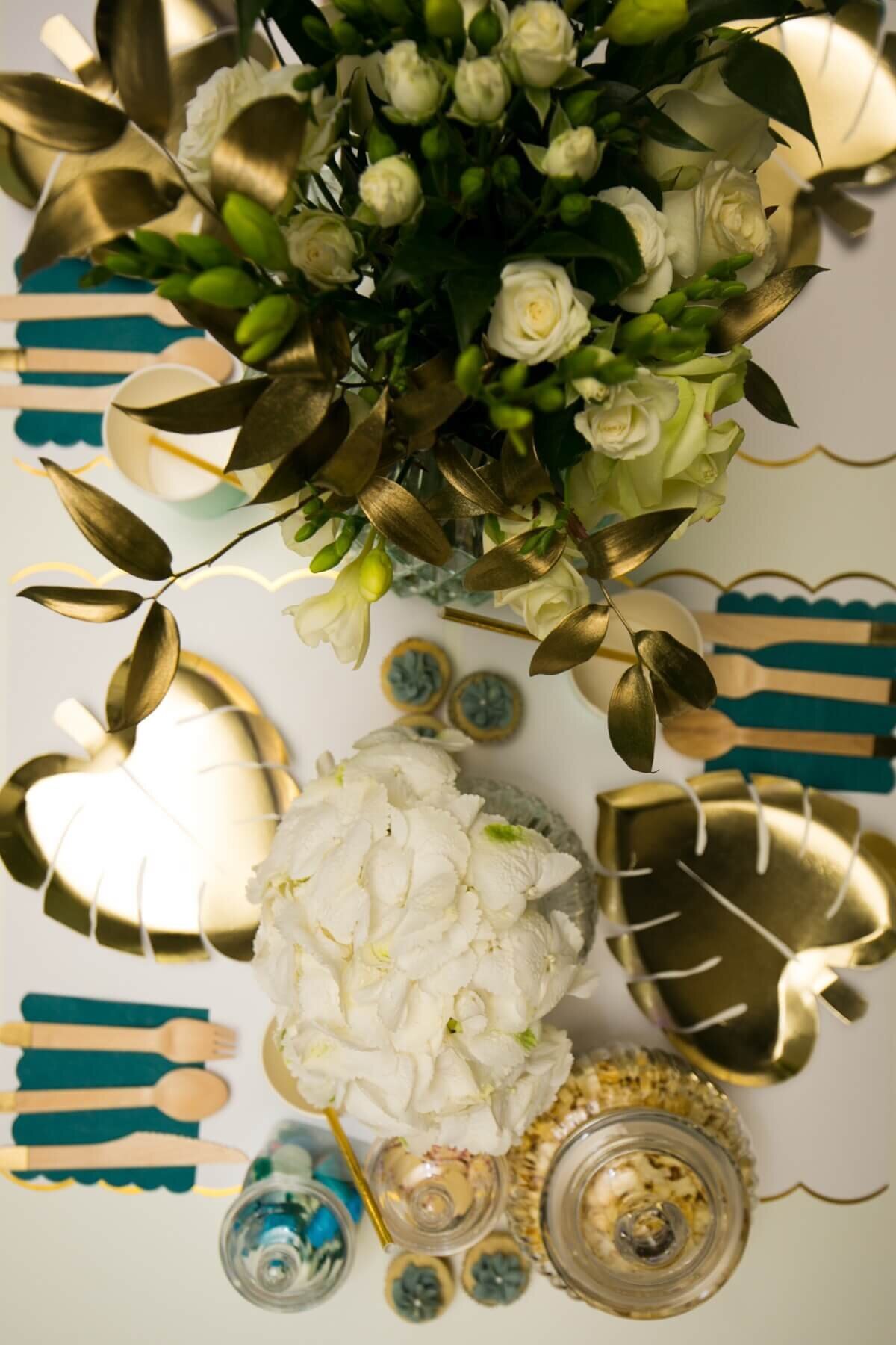 Gold and white children's table setting with sweet jars, flowers and gold leaf plates