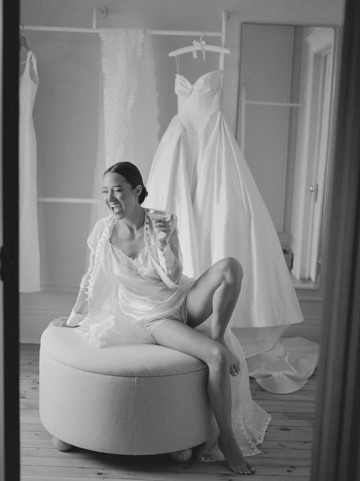a bride laughs in her silk and lace getting ready robe, champagne coupe in-hand, documented poetically by wedding photographer Christina Harrison