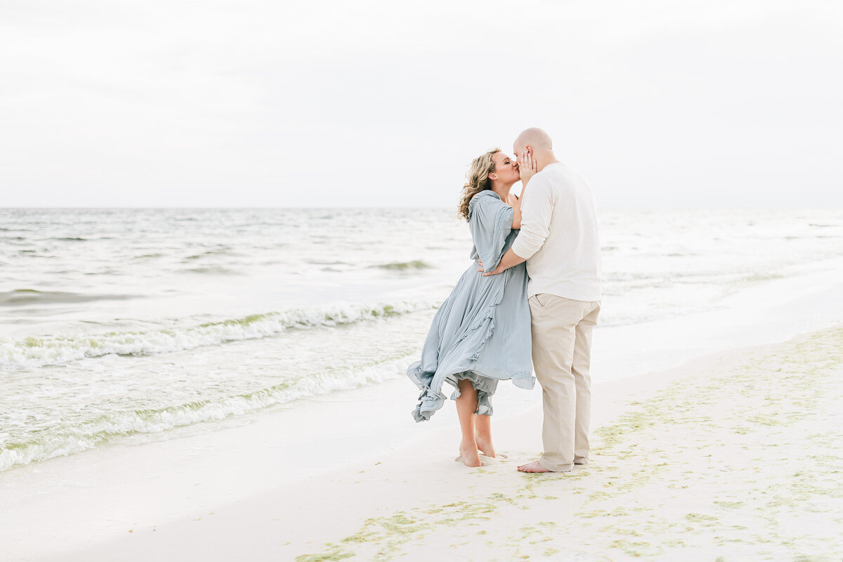 A pair of lovebirds, soon to be parents, sharing a tender kiss on the sandy beach captured by destin maternity photographers.