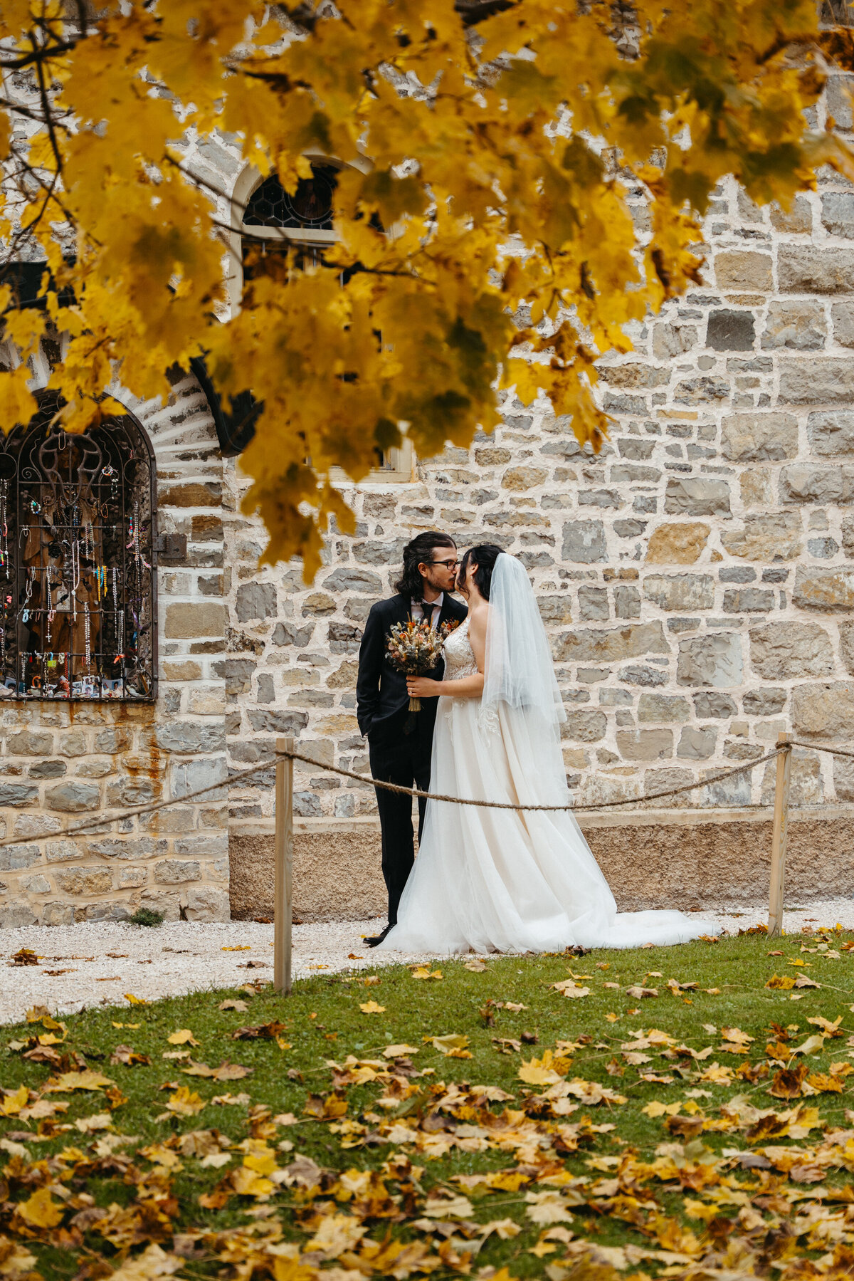 Bride and groom kissing beneath golden autumn trees