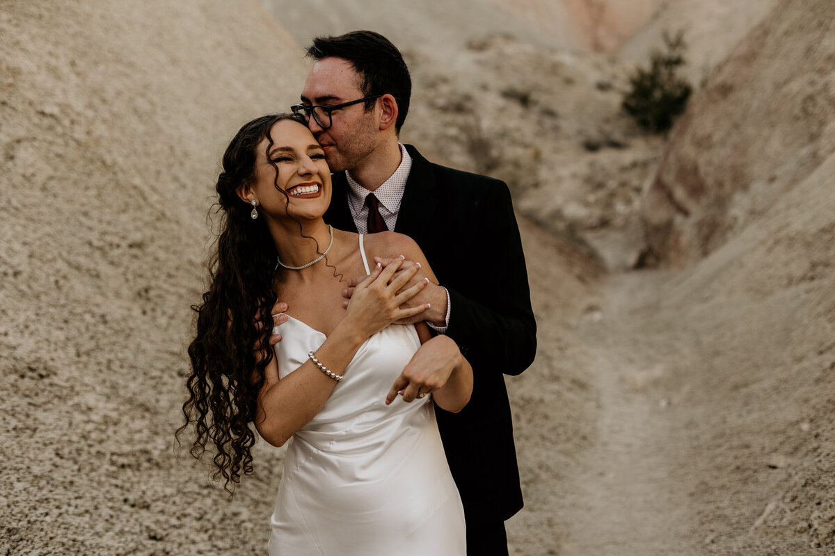 groom hugging bride from behind and whispering to her