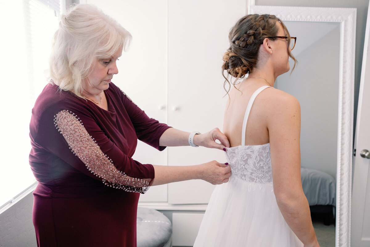 mother of the bride buttons her daughters wedding dress back in the bridal suite at Rosewood Events captured by wedding photographer bay area