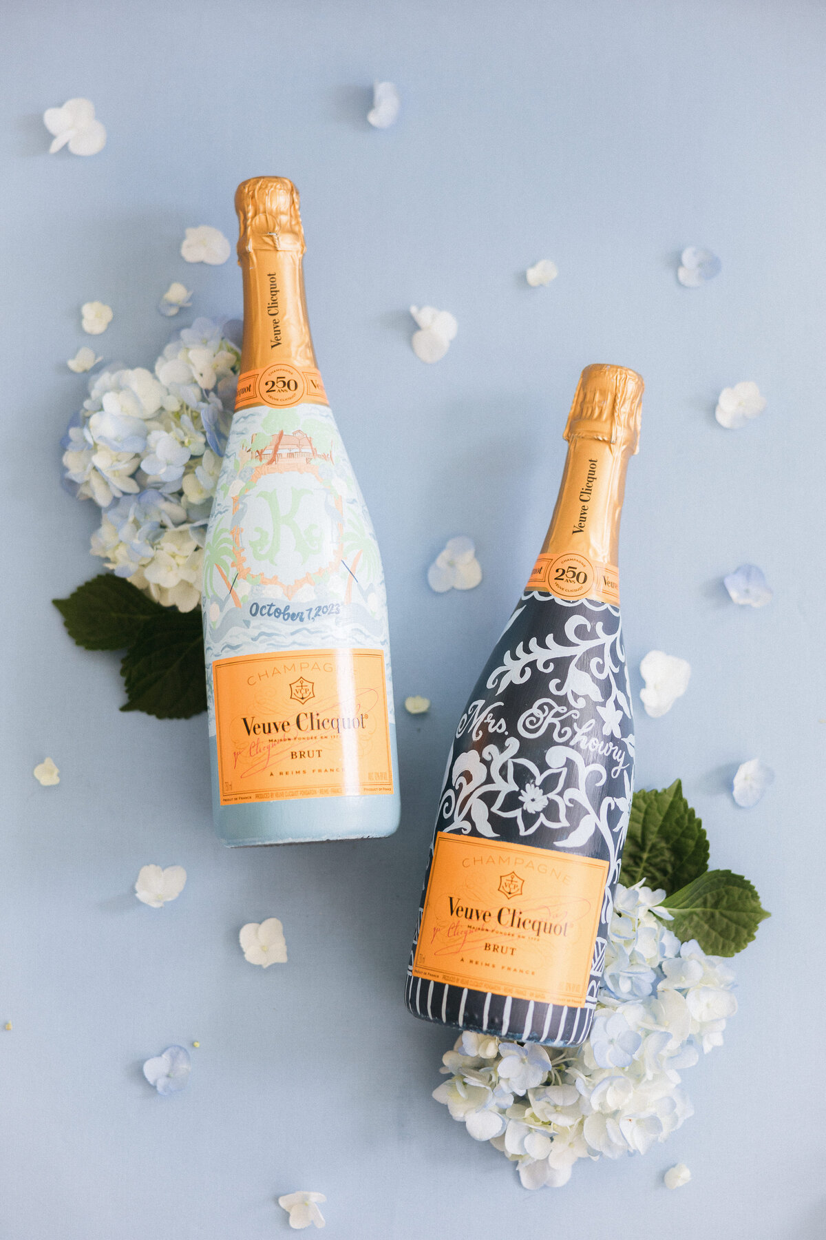 Custom-painted Veuve Clicquot bottles surrounded by blue hydrangea petals—detail from a Bluffton, South Carolina wedding, captured by luxury wedding photographer Amia Marcell.
